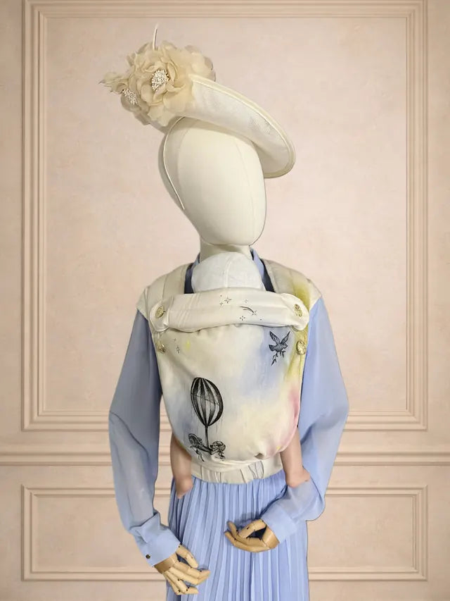 Hand-painted MonDoudou “Toile d’Amour” on a bust wearing a hat, against a panelled wall.