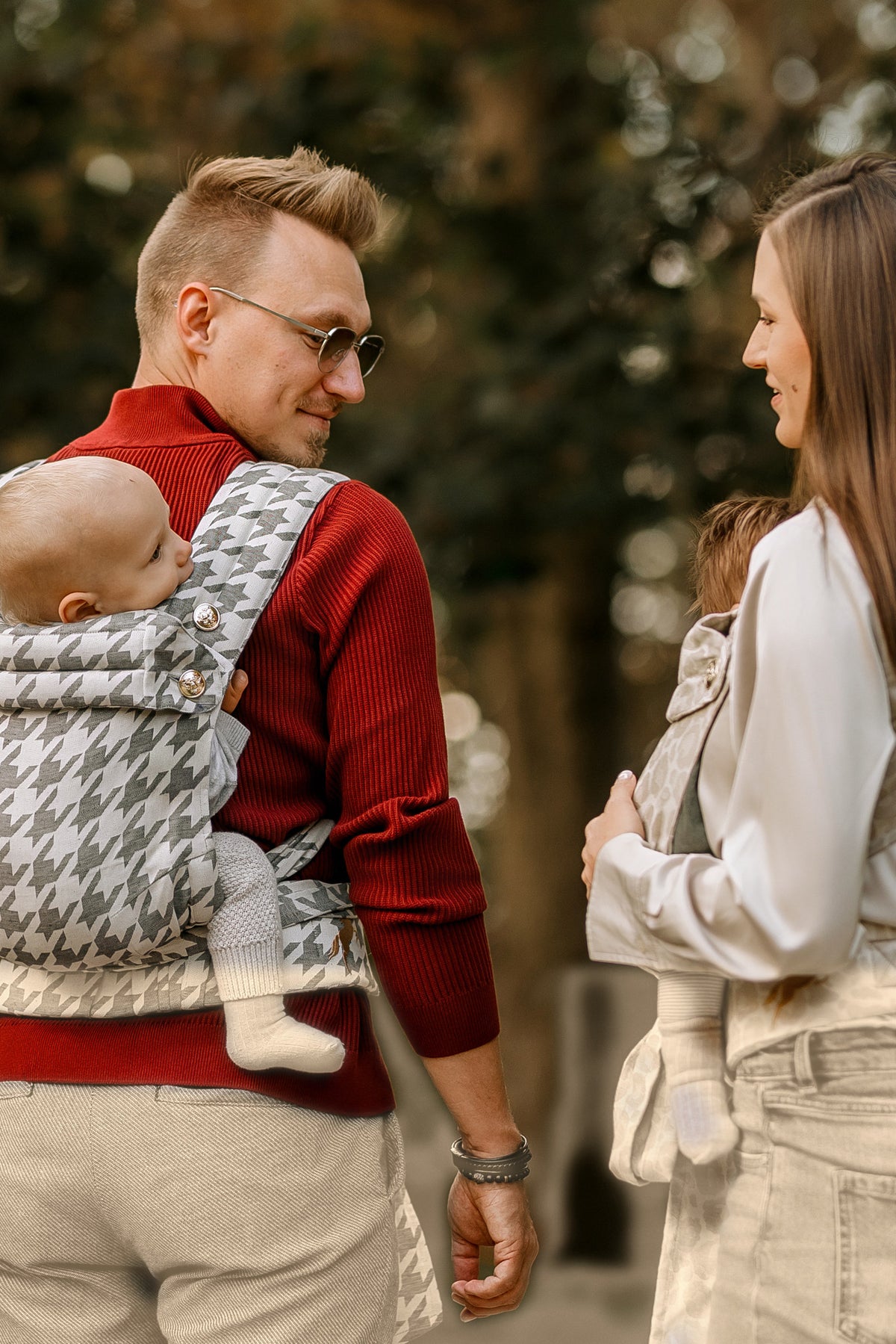 Vater mit Rückentrage und Mutter im Gespräch, das Kind blickt zur Seite.