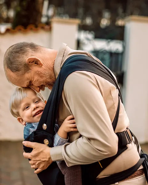 MonDoudou Noir: a man with a grey beard leans towards the laughing child he carries on his front.