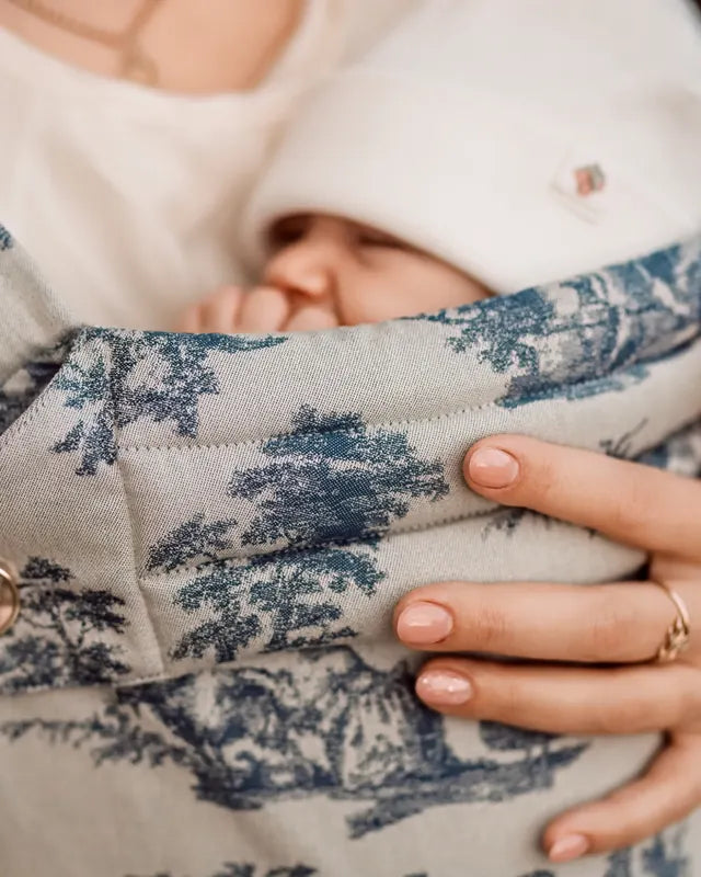 The mother’s hand on the sleeping child, surrounded by the blue motif of the MonDoudou Toile de Jouy.